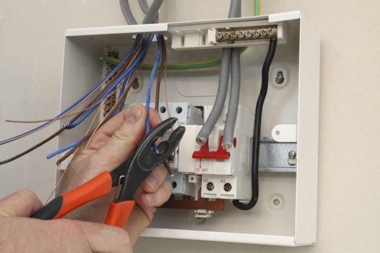 A person using pliers to work on electrical wiring in a junction box.